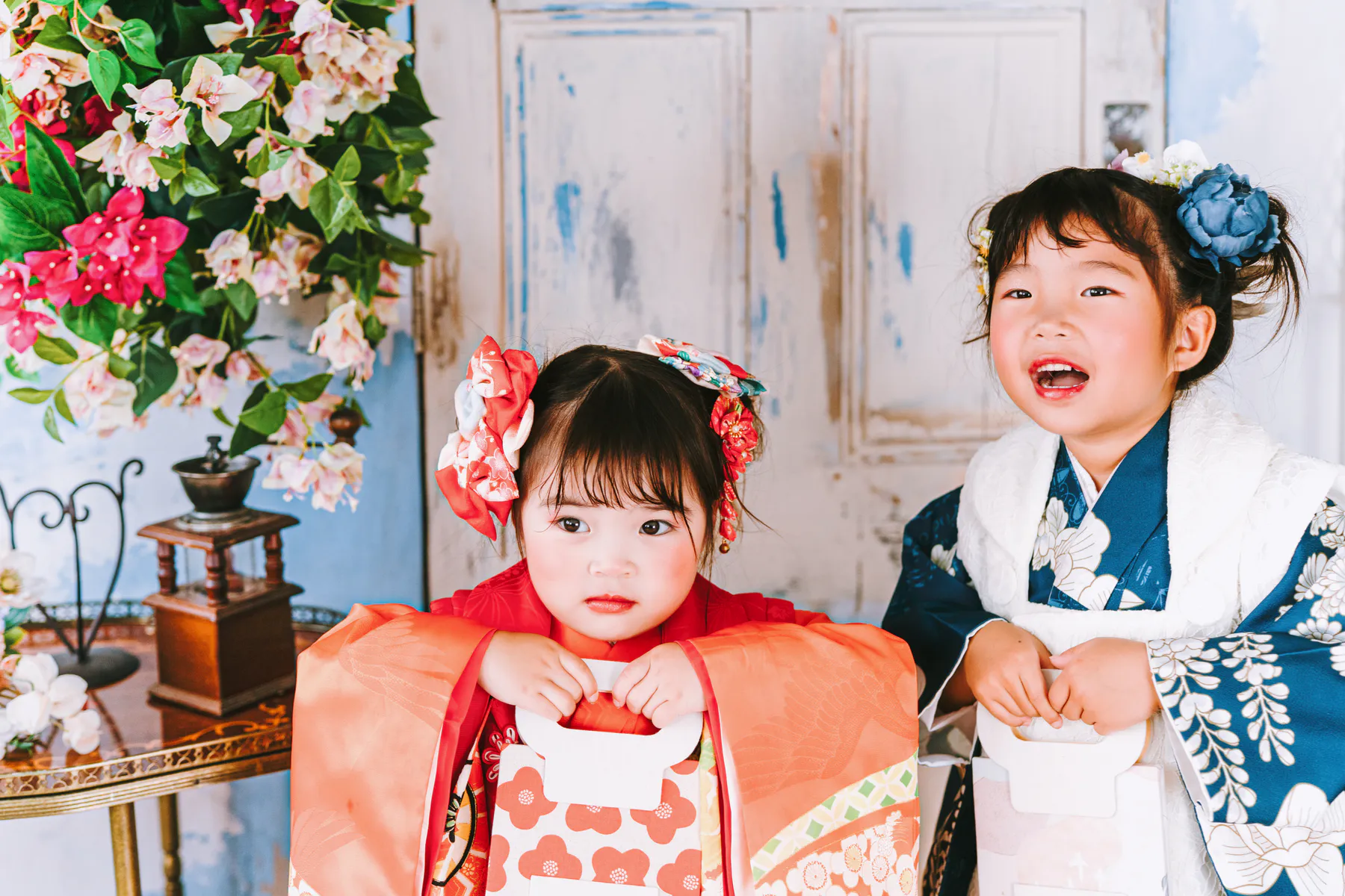 花の咲く空色のアーチの前で、着物の子どもふたりが笑っている